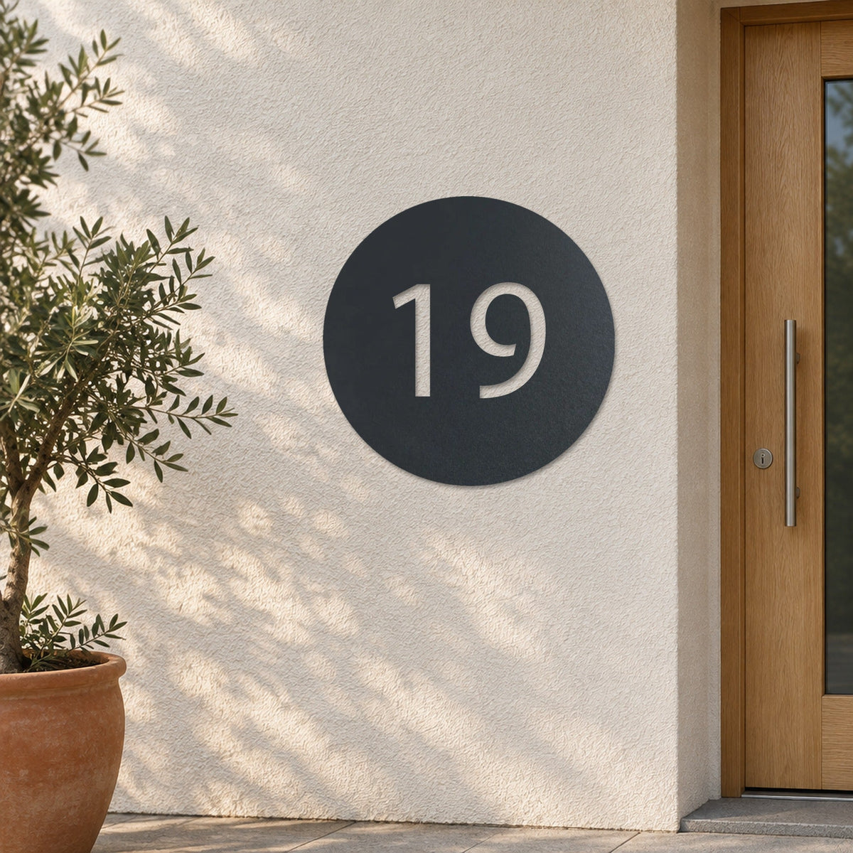 Plăcuță cu număr de casă din inox, personalizată – Număr de casă în cerc „19” pe un perete tencuit deschis la culoare, inox antracit RAL 7016 · MOHAVE